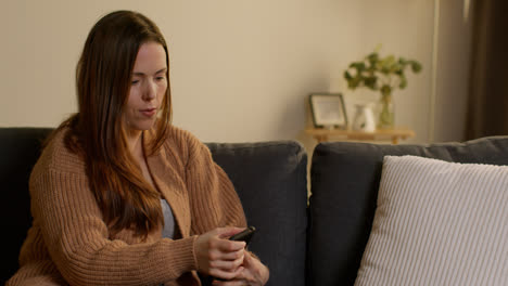 Woman-Sitting-On-Sofa-At-Home-Using-Mobile-Phone-To-Check-Social-Media-Message-And-Scrolling-Online-8